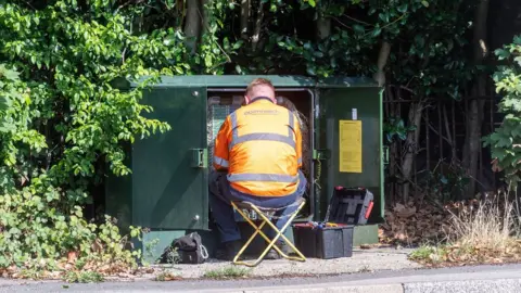 Alamy Engineer working in a green box with communications cables