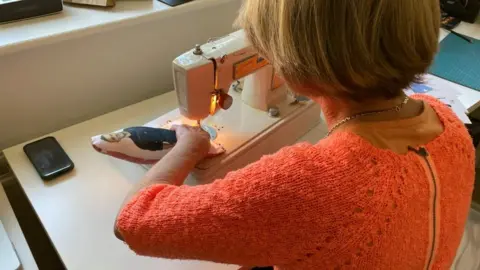 Andy Trigg/BBC Julia Leadbetter sewing a huggable hero toy that she is making on a sewing machine