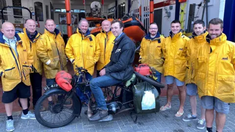 RNLI Harry Bott and his vintage motorbike with members of the Clacton lifeboat crew in Essex