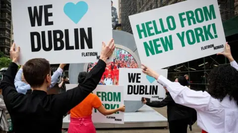 Reuters People hold signs as they greet during the reveal of The Portal, a public technology sculpture that links with direct connection between Dublin, Ireland and the Flatiron district in Manhattan, in New York City, U.S., May 8, 2024.