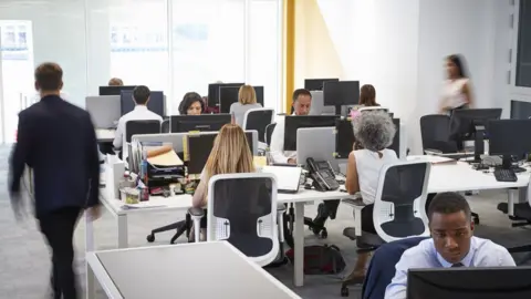 Getty Images Man walking through a busy open plan office