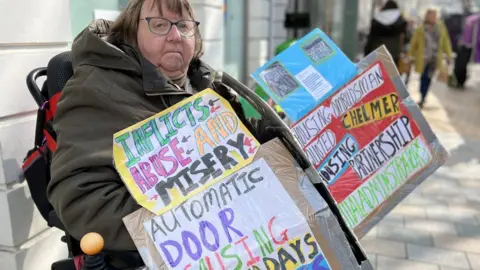 Stuart Woodward/BBC Carol Aldridge on Chelmsford High Street with protest banners