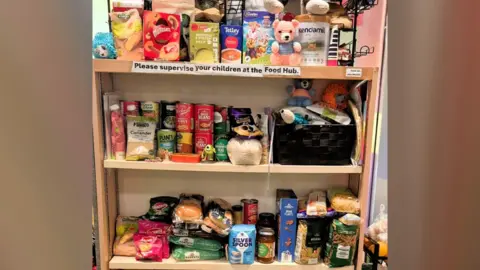 Little Miracles Shelves of food items including boxes of soup, tins and jars placed next to each other.
