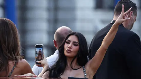 Kim Kardashian poses for a photo on a Venice water taxi. Her fingers are raised in a peace sign.