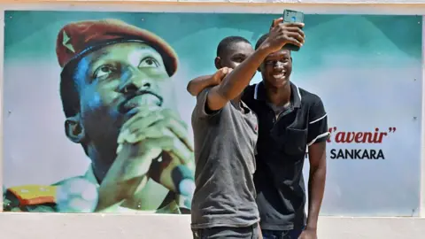AFP Two male students take a photo next to an poster pan-Africanist icon Thomas Sankara at the University Thomas Sankara near Ouagadougou in Burkina Faso - October 2021.