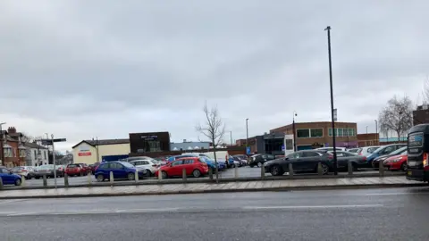 LDRS Picture of Borough Road Car Park in Wakefield City centre. It shows a number of cars parked, with a road in the foreground and buildings in the background. 