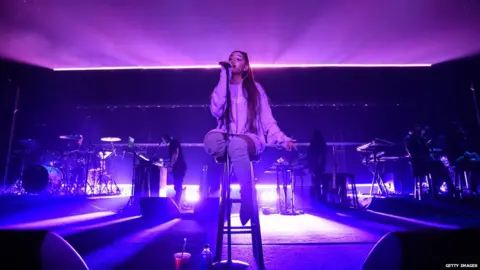 Getty Images Ariana sits and sings