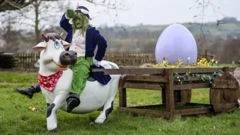 Yony Choi A person in a Grinch costume sitting on a large fake cow