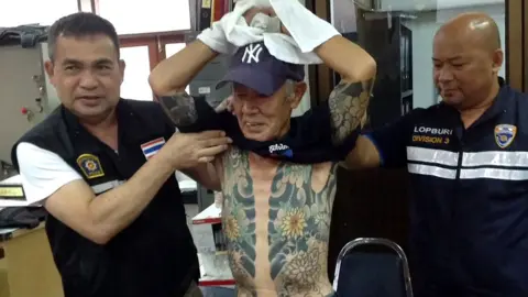 AFP Thai policemen with Mr Shirai, displaying the tattoos on his body