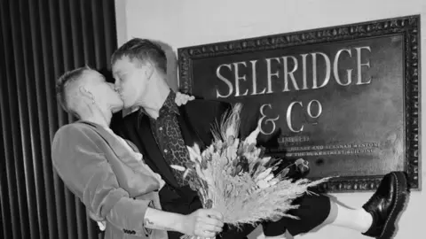 Selfridges Undated handout issued by Selfridges of Marc Gee-Finch (left) and Kampus Tobor kissing in front of a Selfridges sign