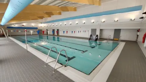 Bob Young An indoor swimming pool with lanes and bunting hung across the room.