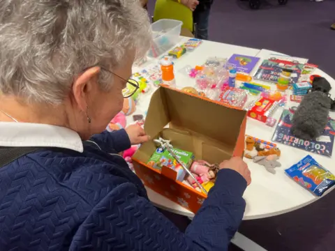 Maureen Summerhayes, wearing a blue jumper, looking at a shoebox as she puts gifts inside it