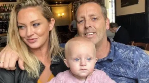 Family handout Michelle left, Theia as a baby in the middle and Theia's dad Edward Papworth on the right they are sat inside.