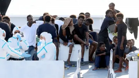 Reuters Migrants wait to disembark Italy's coastguard vessel at the port of Catania. Photo: August 2018