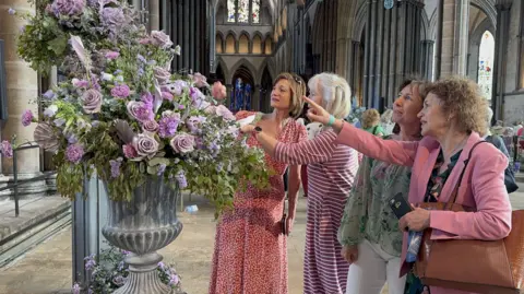 Cheryl Dennis/BBC Four women study a large and intricate floral display which is part of the Salisbury Cathedral Flower Festival