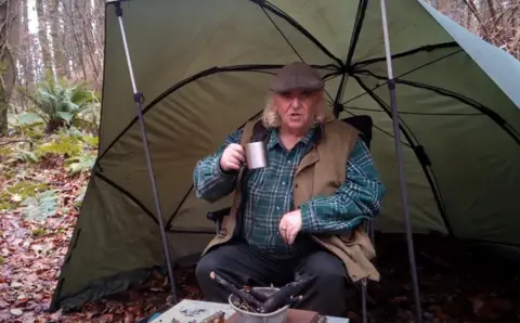 Wander With Mac/YouTube Man sitting with a cup of tea in a tent