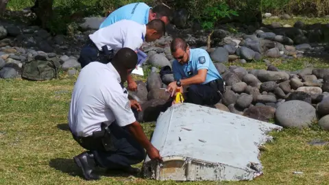 Reuters Police inspect a large piece of plane debris which was found on the beach in Saint-Andre, on the French Indian Ocean island of La Reunion, 29 July 2015