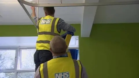 BBC Workmen inspecting the roof of a hospital affected by the RAAC plank problem