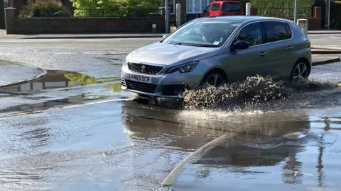 Jill Bennett/BBC Car driving through flooded road