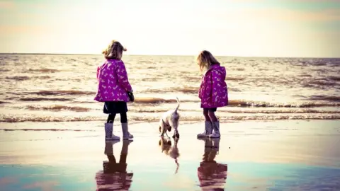 Paul Chandler Two girls stand on beach at Ogmore on Sea with their puppy, Luna