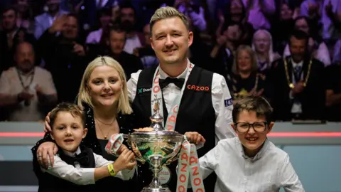 Getty Images Kyren Wilson celebrates with his family in front of the World Championship trophy