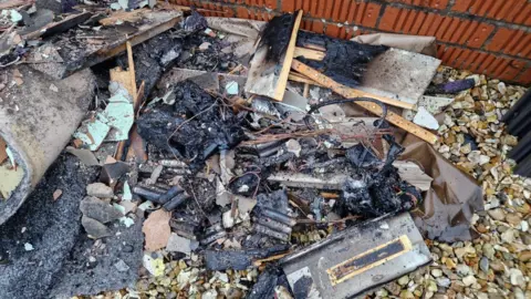 Christine and Neil Clayton A huge pile of black charred debris is outside, resting on a pile of small stones. 