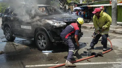Getty Images Two men extinguishing fire of a burnt black car