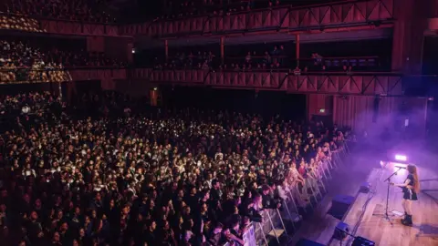 Jessie Myers Holly Humberstone on stage at Bristol Beacon with a wide shot of a crowd in the background