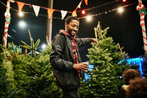 Thomas Barwick/Getty Smiling father shopping for Christmas tree with family