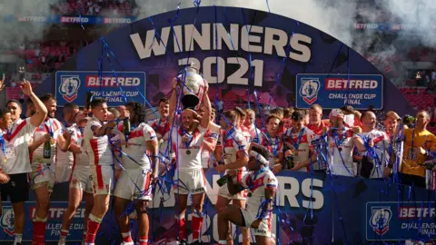 PA Media St Helens' James Roby (centre) holds the trophy as team-mates celebrate after the Betfred Challenge Cup final match