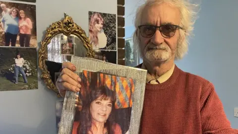 Andrew Turner/BBC Keith Gant holding a framed photo of his late wife