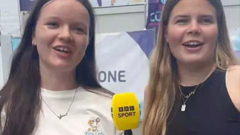 Two women looking into camera and holding BBC Sport-branded microphone