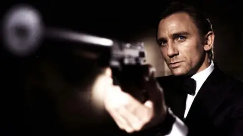 EON Productions Daniel Craig as James Bond. He is seen wearing a tuxedo and pointing a gun off-screen.