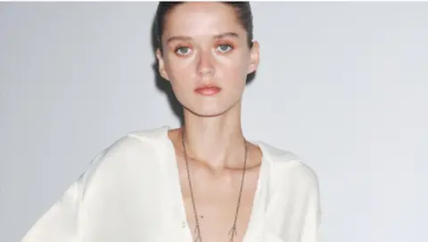 Zara A pale model poses in a white Zara shirt staring at the camera with a blank expression and the low cut design of the top shows her protruding collarbones
