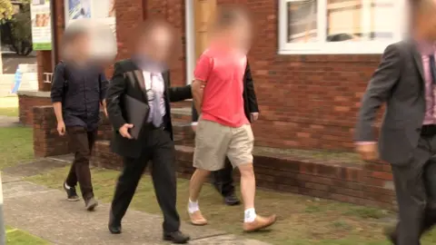 AUSTRALIAN FEDERAL POLICE HANDOUT A man with a blurred face is led away by police officers following his arrest