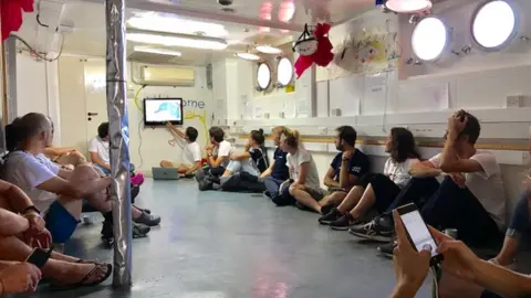 Crew members sit on the floor watching TV