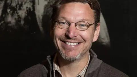 Astronomer Mike Brown standing in front of a picture of a planet