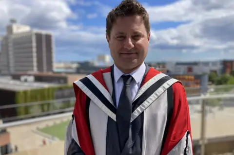 BBC/Dave Edwards George Clarke wearing a university robe