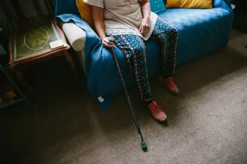 BBC Jackie Cheetham sits at home with her walking stick