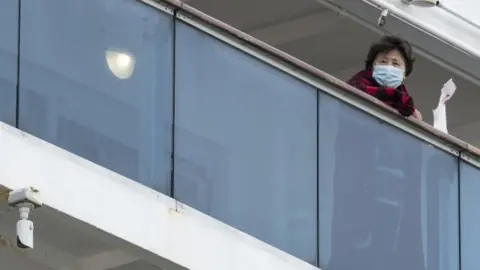 Getty Images A passenger peers out from the Diamond Princess. The company is providing extra TV, films, games, and newspapers for quarantined passengers, plus room service food