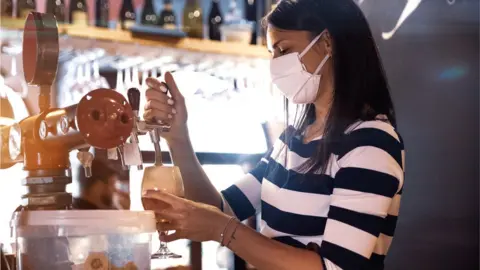 Getty Images A woman pulling a pint wearing a mask