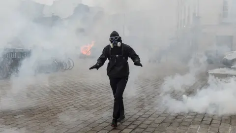 AFP A protester dressed in black walks amid tear gas smoke during a protest against the pension overhauls, in Nantes, on 5 December, 2019.