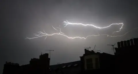 BBC WEATHER WATCHERS - RACH A dark night sky with the silhouette of buildings and a bright white lightning bolt in the sky