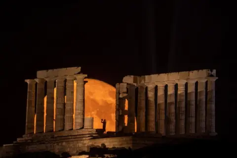 Alkis Konstantinidis / Reuters A person takes a photo as a full moon known as the "Buck Moon" rises behind the Temple of Poseidon, in Cape Sounion, near Athens, Greece