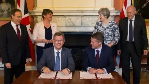 Reuters DUP MP Jeffrey Donaldson and Tory Chief Whip Gavin Williamson sign paperwork as DUP's deputy leader Nigel Dodds, leader Arlene Foster, PM Theresa May and First Secretary of State Damian Green look on.