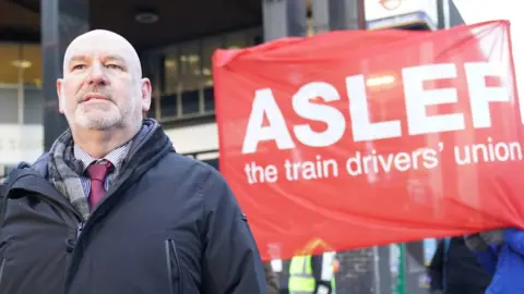 PA Media Mick Whelan of Aslef stands in front of a union banner