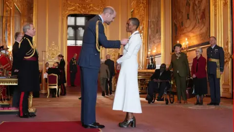 PA Media A man in a navy suit presenting an award to a lady in a white dress. They are at a ceremony inside a castle.