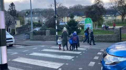 John Wimperis/LDRS Children and parents cross the zebra crossing outside a school