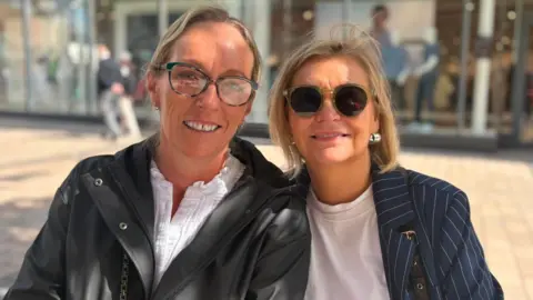 Two blonde women, one wearing glasses and the other sunglasses