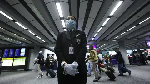 Getty Images A health worker stands by ready to ask passengers to remove head gear prior to temperature screening on April 27, 2009 at the international airport in Hong Kong